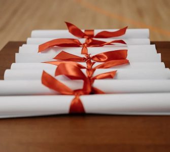 Imagem de diversos certificados enrolados por laços vermelhos, representando a conclusão de cursos ou eventos.