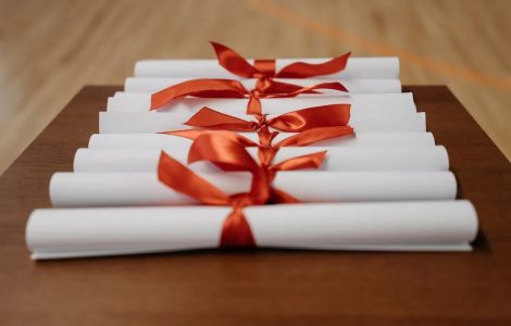 Imagem de diversos certificados enrolados por laços vermelhos, representando a conclusão de cursos ou eventos.