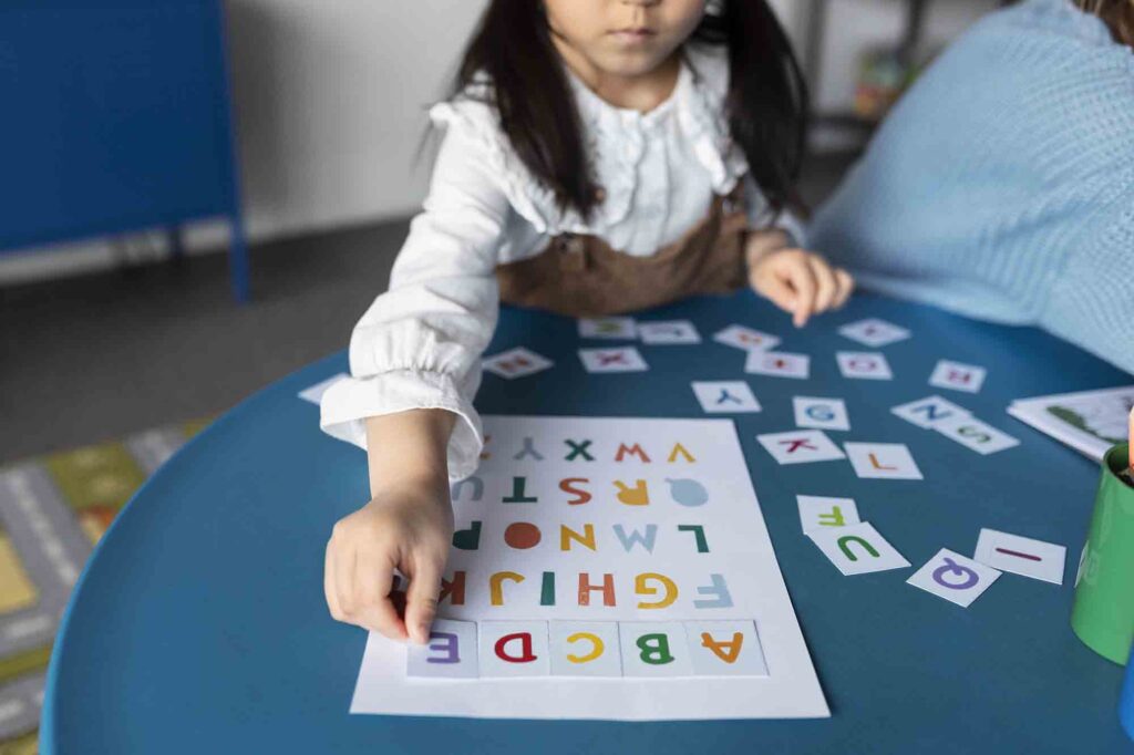 Uma criança sentada em frente a uma mesa azul com uma cartilha de letras