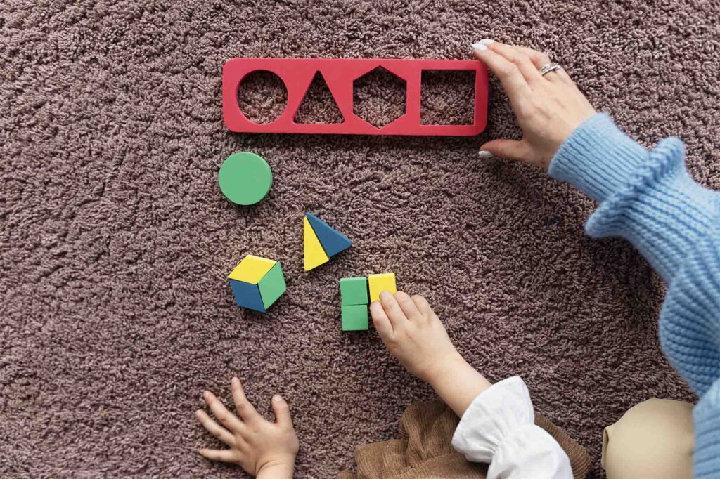Os braços de uma criança acompanhada de um adulto brincando em um tapete com brinquedos educacionais de encaixe coloridos