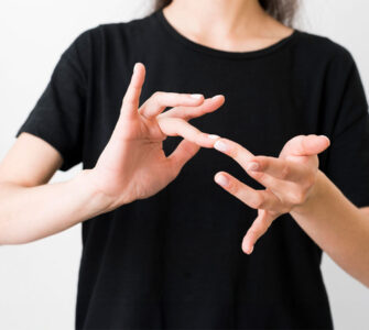 Pessoa vestindo camiseta preta realizando um sinal em Libras com as mãos