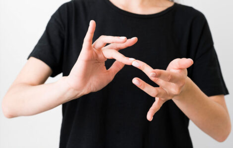 Pessoa vestindo camiseta preta realizando um sinal em Libras com as mãos