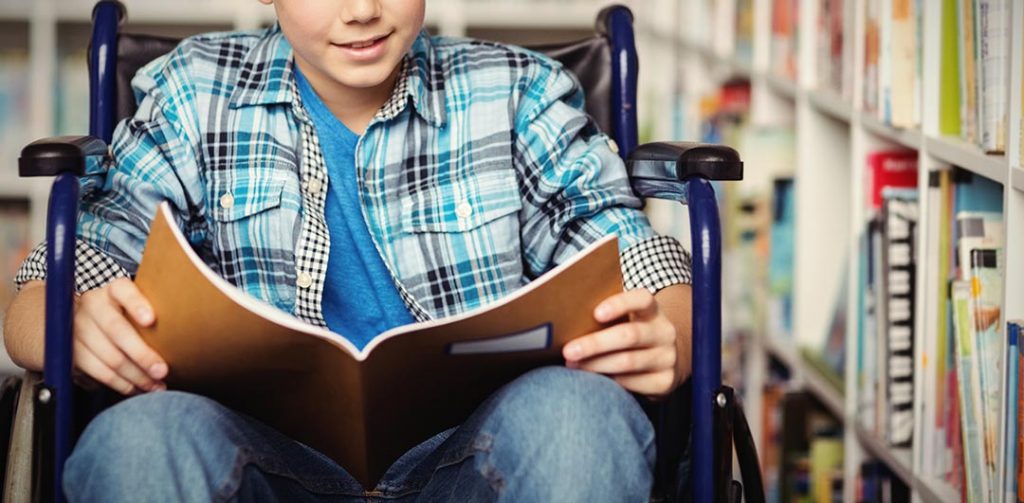 Menino lendo em uma cadeira de rodas