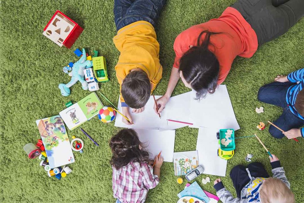 Crianças colorindo na grama com brinquedos espalhados