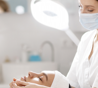Profissional esteticista realizando tratamento na pele de uma cliente, deitada em sua frente, em ambiente clínico.