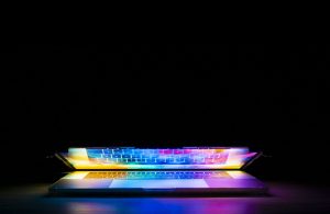  Imagem com fundo preto, ilustrando um laptop entreaberto e destacado pela iluminação de diversas cores.