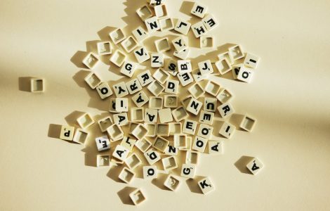 Imagem de diversos pequenos blocos de plástico ilustrados por letras do alfabeto, jogadas e desordenadas em fundo amarelado.