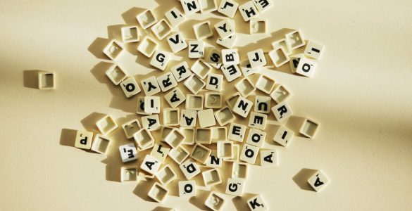 Imagem de diversos pequenos blocos de plástico ilustrados por letras do alfabeto, jogadas e desordenadas em fundo amarelado.