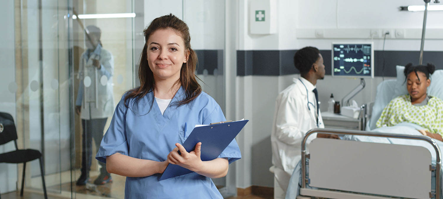 Médica com leve sorriso e uma prancheta a frente de um paciente em uma maca.