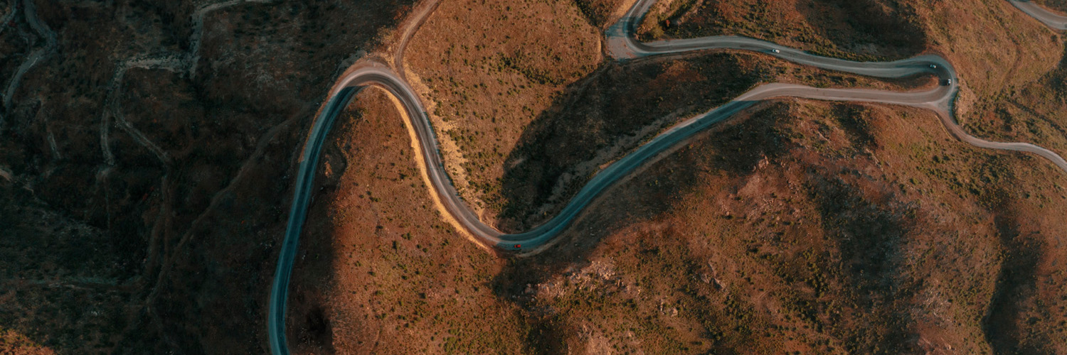 Terreno de colinas com vegetação amarronzada e uma estrada central