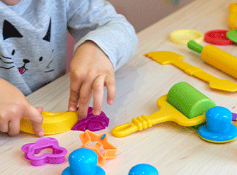 Criança de roupa cinza brincando em uma mesa utilizando diversos materiais coloridos
