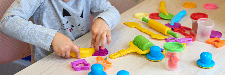 Criança de roupa cinza brincando em uma mesa utilizando diversos materiais coloridos