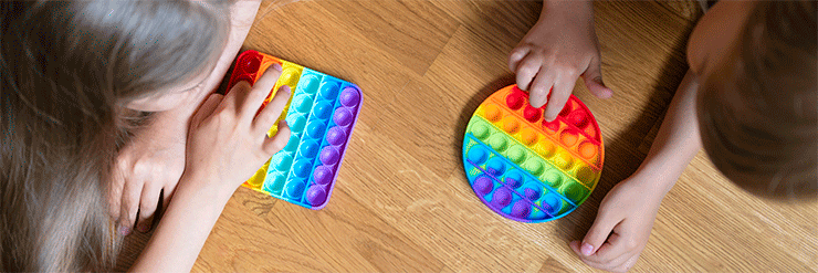 Duas crianças no chão brincando com pop-it colorido