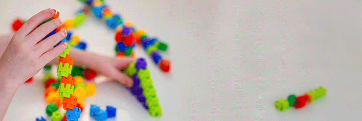 A mão de uma criança é mostrada brincando de encaixar peças de plástico vibrantes e coloridas