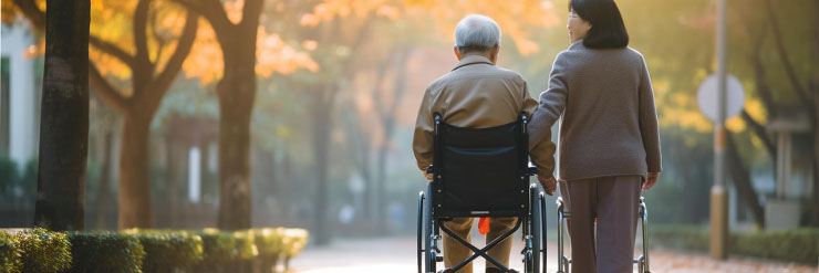 Cuidadora acompanhando idoso em cadeira de rodas durante um passeio em um parque arborizado