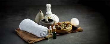 Arranjo de toalhas brancas, óleos cosméticos, folhas secas e pedras sob uma tábua de madeira. Imagem em fundo escuro