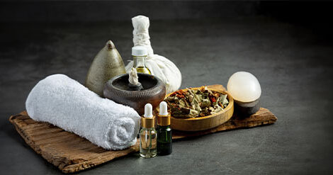 Arranjo de toalhas brancas, óleos cosméticos, folhas secas e pedras sob uma tábua de madeira. Imagem em fundo escuro