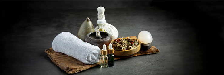Arranjo de toalhas brancas, óleos cosméticos, folhas secas e pedras sob uma tábua de madeira. Imagem em fundo escuro