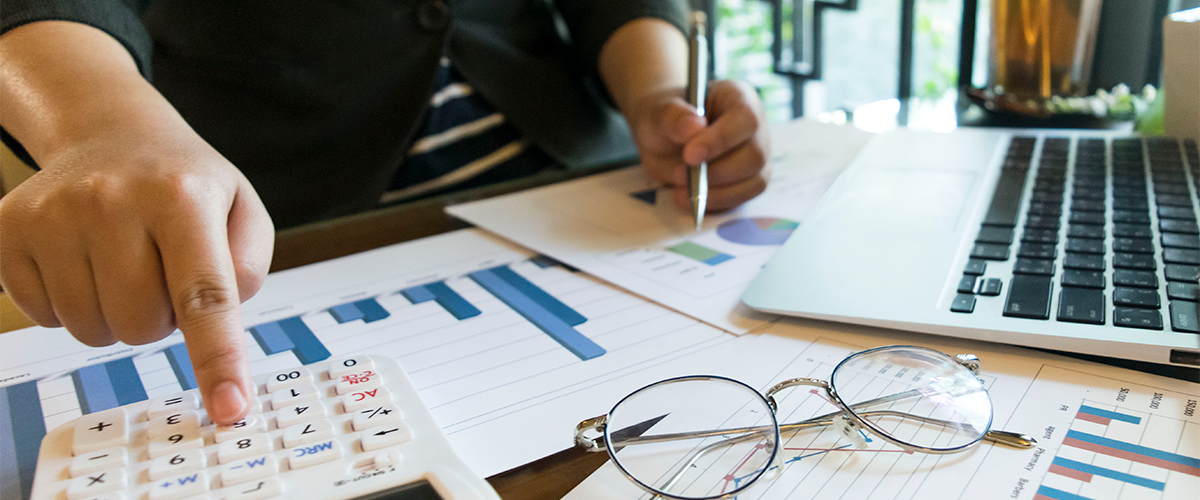 Pessoa utilizando uma calculadora enquanto analisa gráficos e dados financeiros com um laptop ao lado, representando a análise financeira