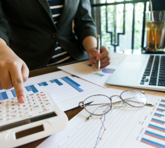 Pessoa utilizando uma calculadora enquanto analisa gráficos e dados financeiros com um laptop ao lado, representando a análise financeira