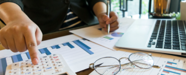 Pessoa utilizando uma calculadora enquanto analisa gráficos e dados financeiros com um laptop ao lado, representando a análise financeira