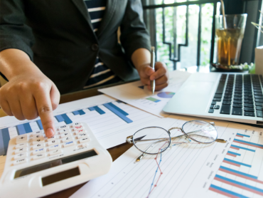 Pessoa utilizando uma calculadora enquanto analisa gráficos e dados financeiros com um laptop ao lado, representando a análise financeira