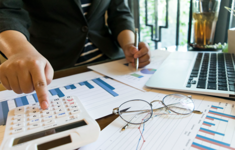 Pessoa utilizando uma calculadora enquanto analisa gráficos e dados financeiros com um laptop ao lado, representando a análise financeira