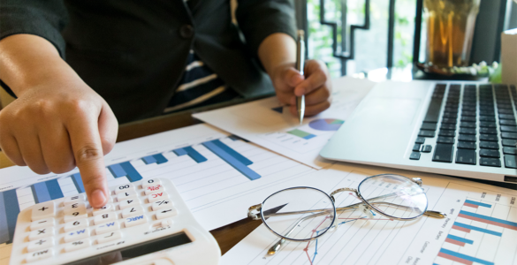 Pessoa utilizando uma calculadora enquanto analisa gráficos e dados financeiros com um laptop ao lado, representando a análise financeira