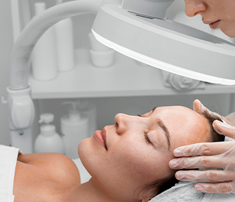 Visagista realizando análise facial em paciente deitada, utilizando lupa para exame detalhado