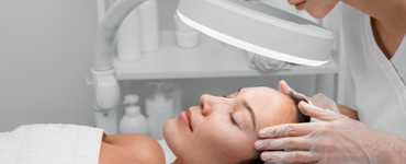 Visagista realizando análise facial em paciente deitada, utilizando lupa para exame detalhado