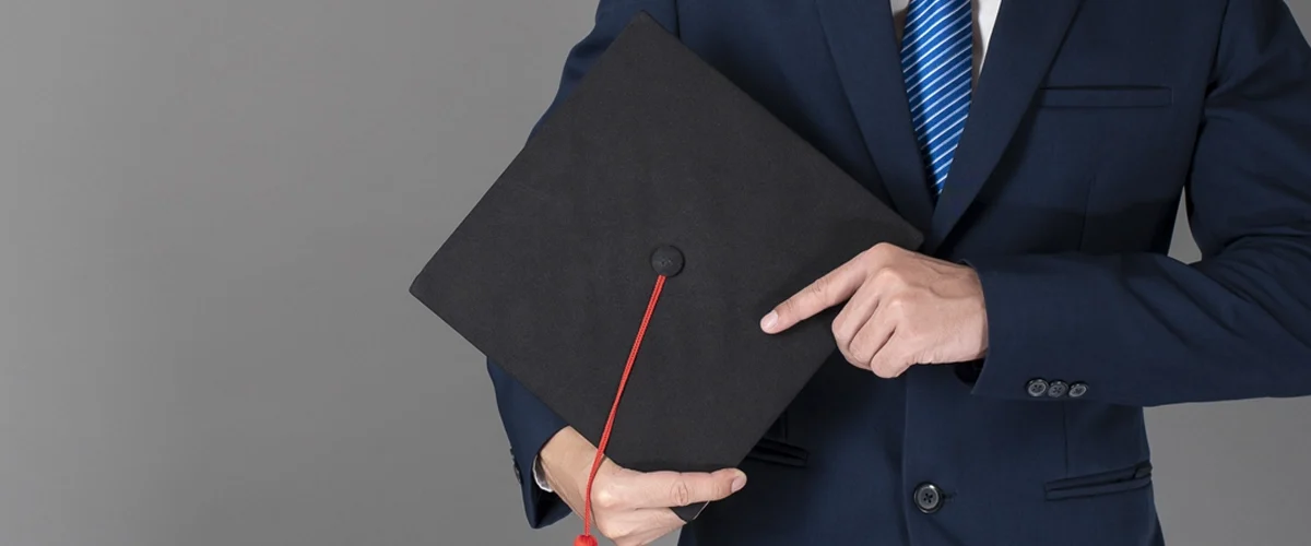 Homem de terno segurando um capelo de formatura preto com uma faixa vermelha, simbolizando a conclusão de um curso de pós-graduação ou MBA.