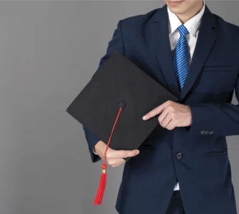 Homem de terno segurando um capelo de formatura preto com uma faixa vermelha, simbolizando a conclusão de um curso de pós-graduação ou MBA.