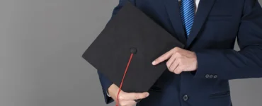 Homem de terno segurando um capelo de formatura preto com uma faixa vermelha, simbolizando a conclusão de um curso de pós-graduação ou MBA.