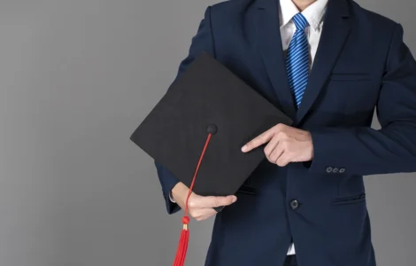 Homem de terno segurando um capelo de formatura preto com uma faixa vermelha, simbolizando a conclusão de um curso de pós-graduação ou MBA.