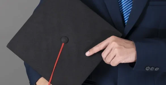 Homem de terno segurando um capelo de formatura preto com uma faixa vermelha, simbolizando a conclusão de um curso de pós-graduação ou MBA.