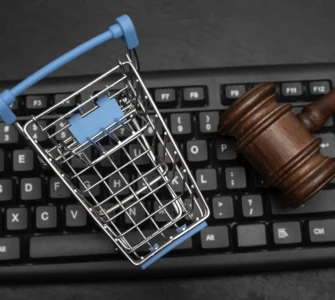 Carrinho de compras em miniatura e martelo de juiz sobre teclado, representando o Direito do Consumidor e o comércio eletrônico.