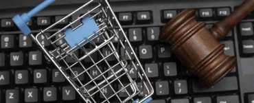 Carrinho de compras em miniatura e martelo de juiz sobre teclado, representando o Direito do Consumidor e o comércio eletrônico.