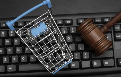 Carrinho de compras em miniatura e martelo de juiz sobre teclado, representando o Direito do Consumidor e o comércio eletrônico.