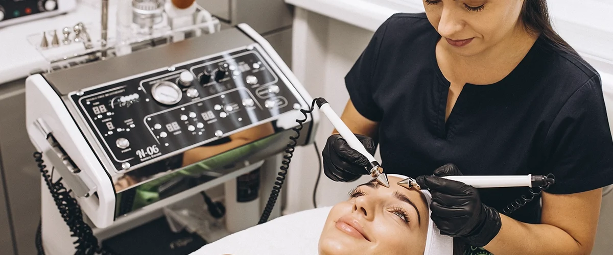 Profissional biomédico esteticista realizando tratamento facial com equipamentos modernos em uma clínica estética.