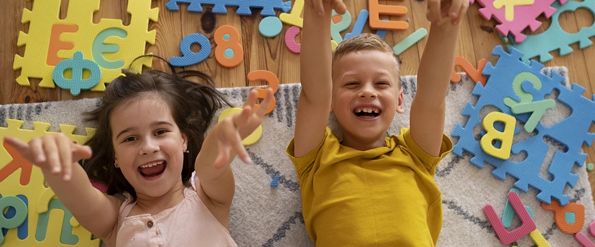 Crianças sorrindo e brincando com peças de encaixe coloridas em formato de letras, estimulando o aprendizado lúdico.