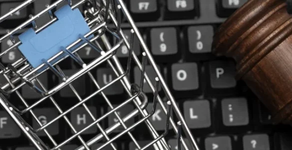 Carrinho de compras em miniatura e martelo de juiz sobre teclado, representando o Direito do Consumidor e o comércio eletrônico.