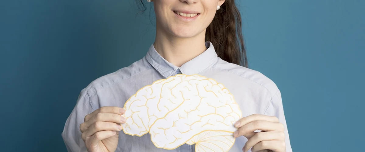Mulher segurando uma ilustração de um cérebro amarelo, sorrindo, em frente a um fundo azul.