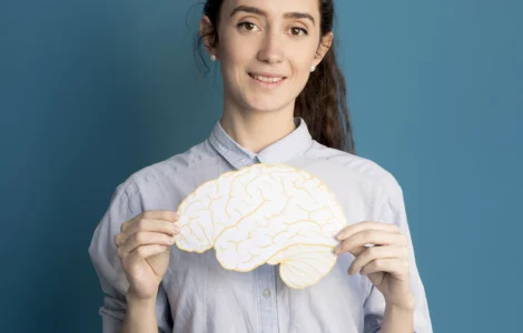 Mulher segurando uma ilustração de um cérebro amarelo, sorrindo, em frente a um fundo azul.