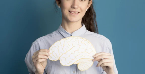 Mulher segurando uma ilustração de um cérebro amarelo, sorrindo, em frente a um fundo azul.