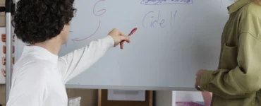 Professores apontando para lousa branca com desenhos organizacionais coloridos representando planejamento pedagógico.