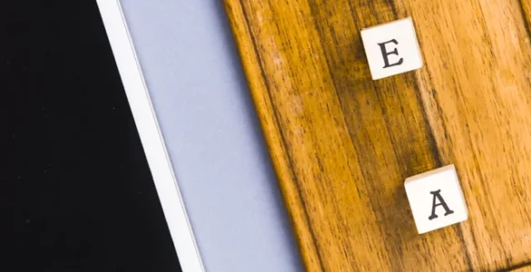 Tablet branco, tabuleiro de madeira com letras formando "TEA" e pratos de porcelana azul sobre fundo lilás.