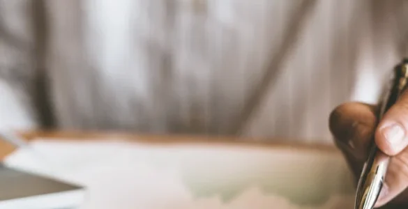 Pessoa trabalhando com documentos, tablet, laptop e calculadora sobre a mesa em ambiente de escritório.