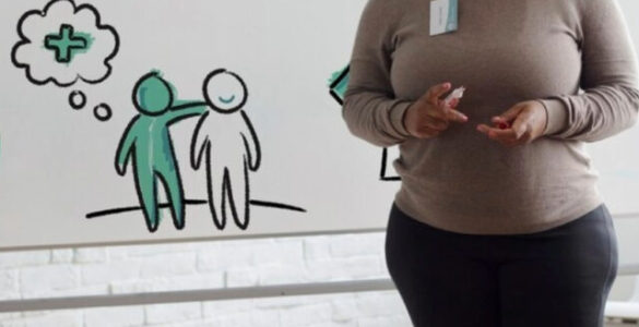 Palestrante apresenta conteúdo sobre Psicologia em sala com grupo e quadro ilustrado ao fundo.