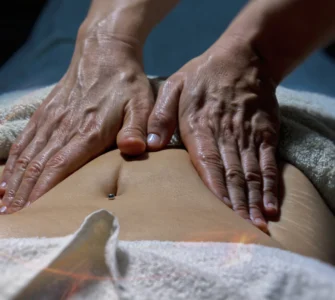 Massoterapeuta realizando massagem abdominal em pessoa deitada com toalha, em ambiente de spa.
