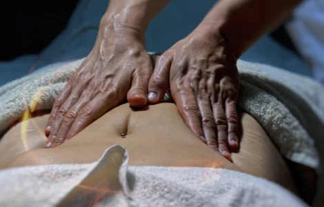 Massoterapeuta realizando massagem abdominal em pessoa deitada com toalha, em ambiente de spa.